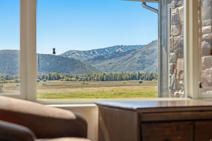 Expansive mountain and meadow scenery framed by a window, featuring a stone exterior wall