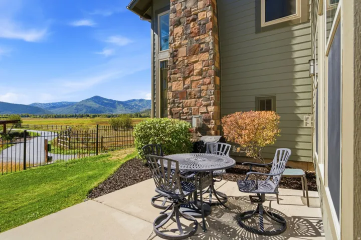 Concrete patio with an expansive grassy area, bordered by a black metal fence, overlooking a vast natural landscape and distant mountains