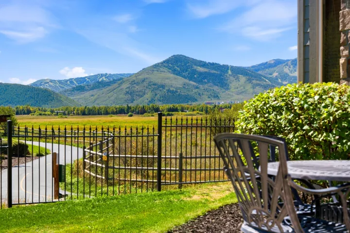 Expansive mountain scenery, lush green valley, manicured lawn, decorative metal fencing, and paved pathway