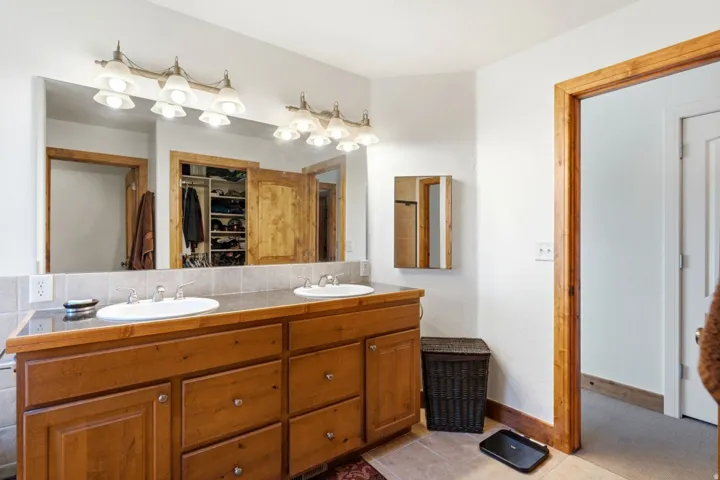 Dual vanity with wood cabinetry, integrated sinks, a wide mirror, and tile backsplash
