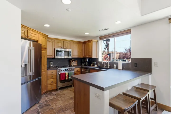 Kitchen featuring wood cabinetry, stainless steel appliances, stone-finish countertops, tile flooring, and recessed lighting