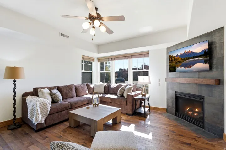 Spacious living area featuring wood-finish flooring, a ceiling fan with integrated lighting, and multiple windows