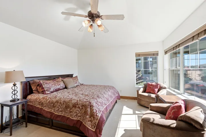 Vaulted ceiling with a ceiling fan, multiple windows with blinds, and carpet flooring
