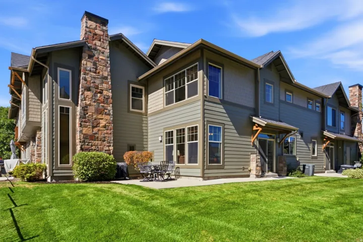 Exterior featuring stone masonry accents, multiple windows, an outdoor patio, and a well-maintained lawn
