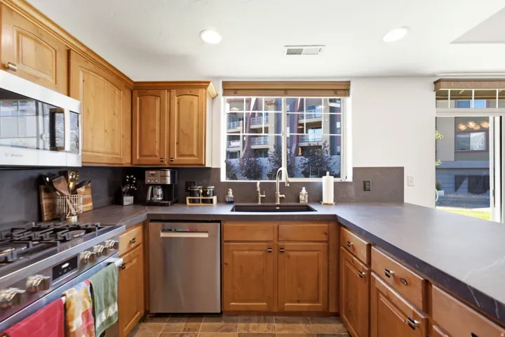 U-shaped kitchen featuring wood cabinetry, stone countertops, stainless steel appliances, and tile flooring