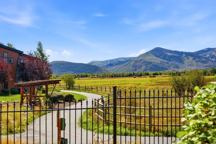 Expansive mountain scenery framing a paved pathway, bordered by a decorative metal fence and natural wood fencing