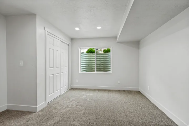 Neutral gray carpeted flooring, a window with a well guard, and white bi-fold closet doors