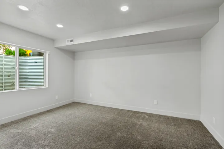 Recessed lighting, light gray carpeting, neutral wall color, white trim, and a window with a window well