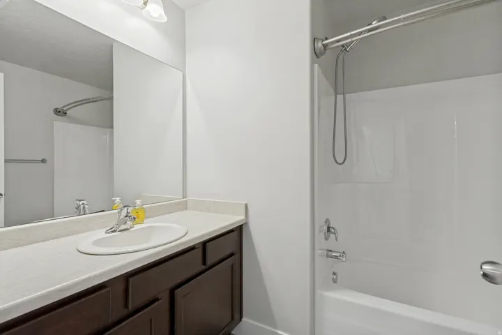 White tub and shower combination with chrome fixtures, a dark wood-finish vanity, and a light-toned countertop with an integrated sink
