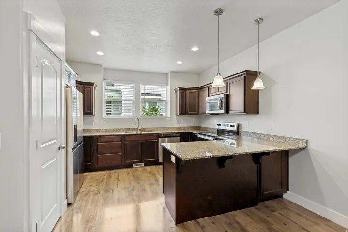 Kitchen featuring dark wood cabinetry, light-toned granite countertops, stainless steel appliances, wood-finish flooring, and recessed lighting