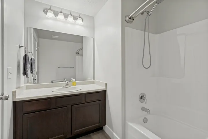 Bathroom featuring a dark wood-finish vanity, light-toned countertop, integrated sink, and a white tub with shower