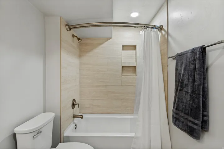 Bathtub with tiled surround, dual recessed shower niches, and bronze-finish fixtures