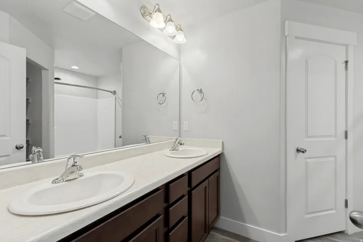 Dual vanity with undermount sinks, brown wood-finish cabinetry, and a full-width wall mirror