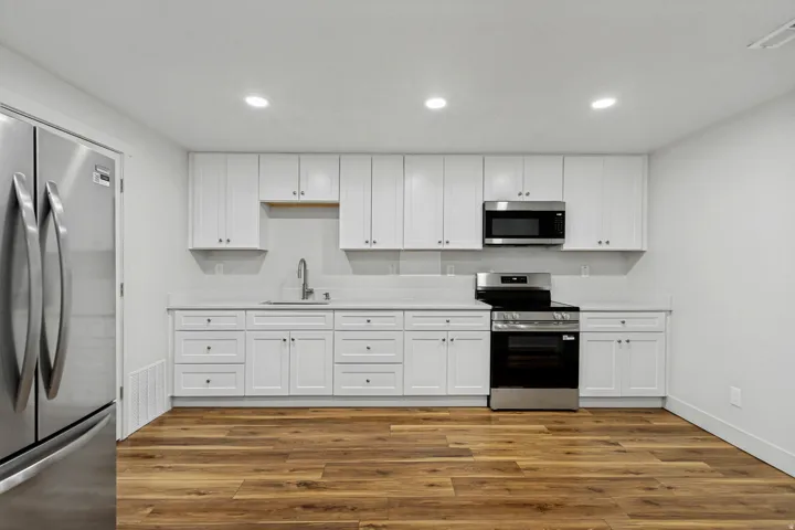 Kitchen featuring stainless steel appliances, white cabinetry, a single basin sink, and wood-finish flooring