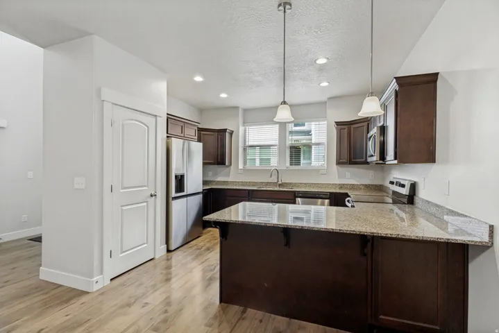 Kitchen featuring wood-finish flooring, dark wood cabinetry, light-toned countertops, and stainless steel appliances