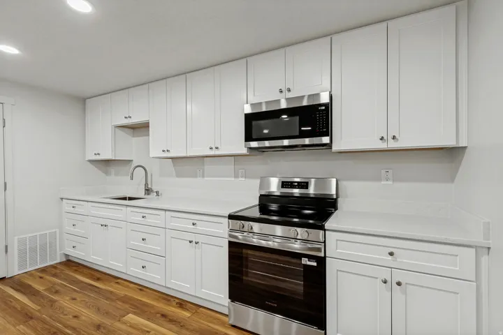 White shaker cabinetry, light countertops, wood-finish flooring, stainless steel range, and built-in microwave