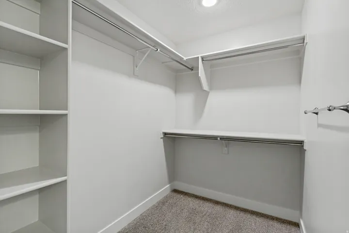 Recessed lighting illuminates a well-appointed closet featuring built-in shelving, multiple hanging rods, and neutral-toned carpeting