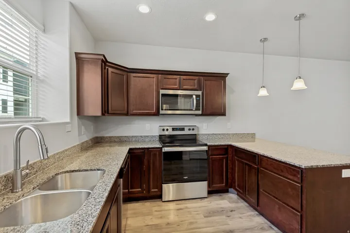 Kitchen featuring rich wood cabinetry, granite countertops, stainless steel appliances, and wood-finish flooring