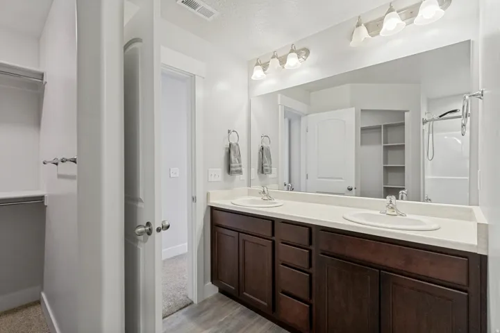 Dual vanity with wood-finish cabinetry, light-toned countertop, and integrated sinks