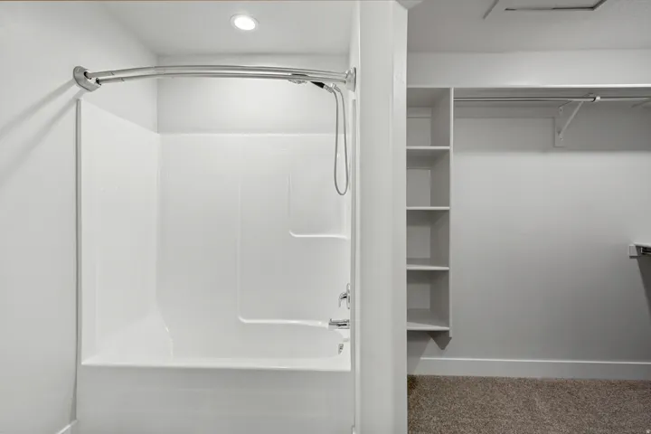 White shower-over-tub combination with a curved shower rod and ceiling-mounted recessed lighting