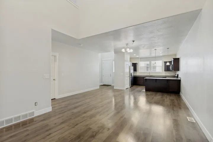 Expansive open-concept living area with wood-finish flooring, a vaulted ceiling, and recessed lighting, flowing into a kitchen featuring dark wood cabinetry, a center island, and pendant lighting