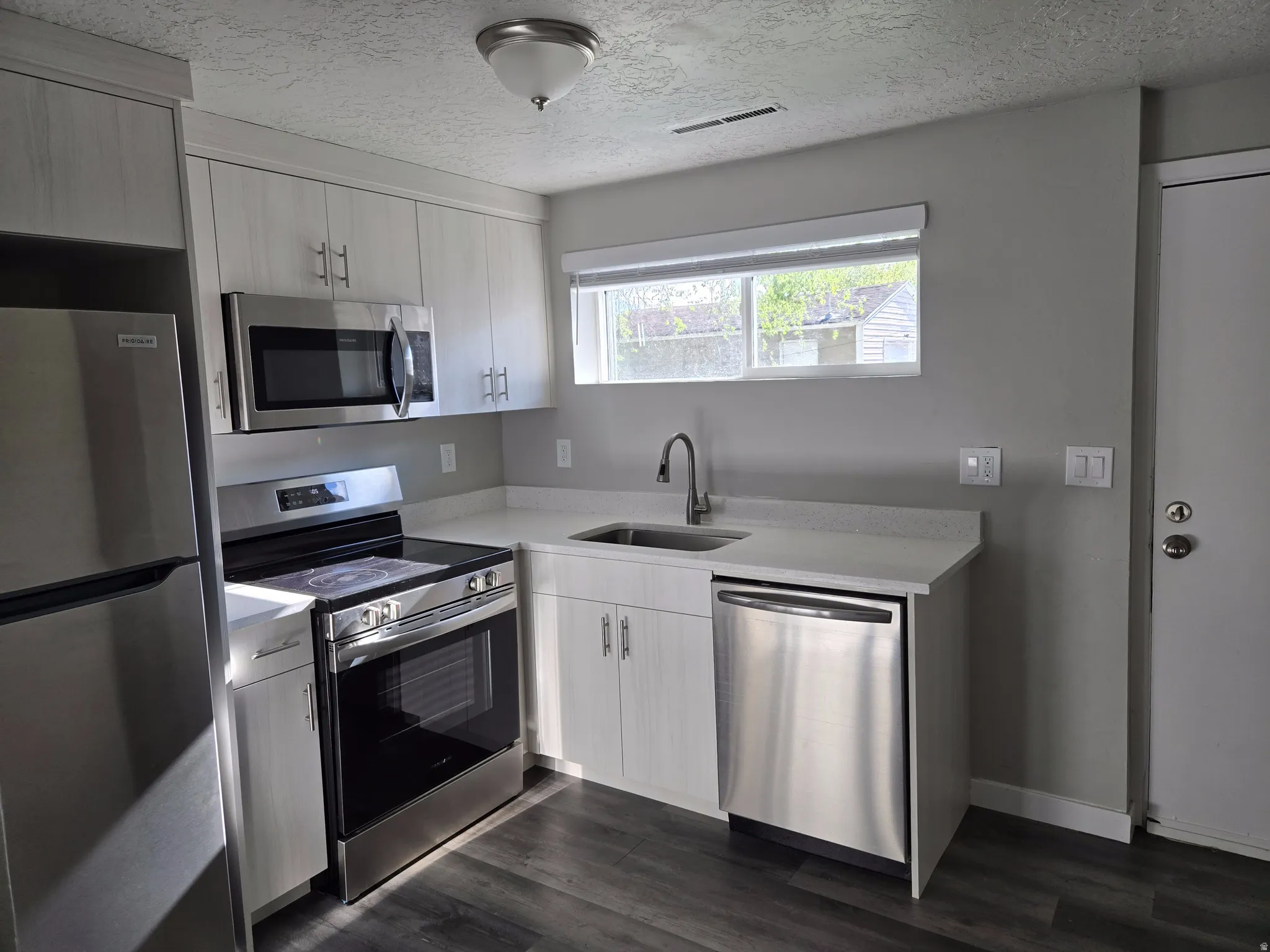 Kitchen featuring a stainless steel appliance suite, light wood-finish cabinetry, light-toned countertops, and wood-finish flooring
