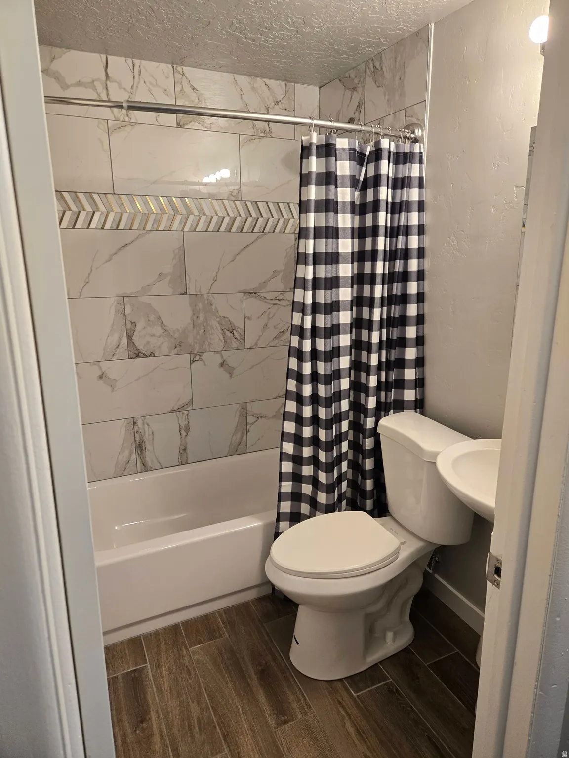 Full bathroom featuring wood-finish flooring, a white porcelain tub, and a shower surround with decorative tile accents