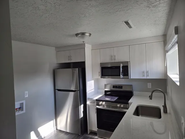 Full-sized stainless steel refrigerator, stainless steel range and overhead microwave, stainless steel sink with a gooseneck faucet, light-toned countertops, and wood-finish cabinetry