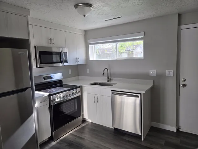 Kitchen featuring a stainless steel appliance suite, light wood-finish cabinetry, light-toned countertops, and wood-finish flooring