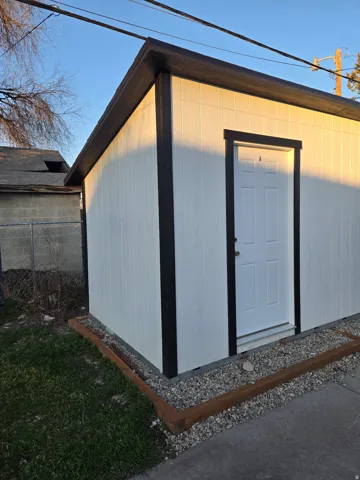 Exterior storage structure with white panel siding and dark trim