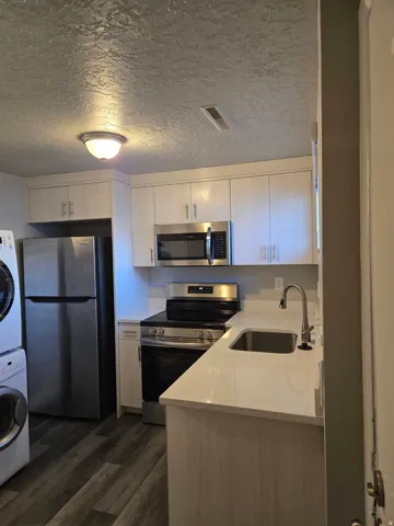 White cabinetry with brushed nickel hardware, stainless steel appliances, light-toned countertops, and wood-finish flooring