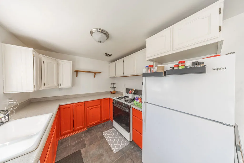 White upper cabinetry contrasting with orange lower cabinetry, light-toned countertops, and dark tile flooring