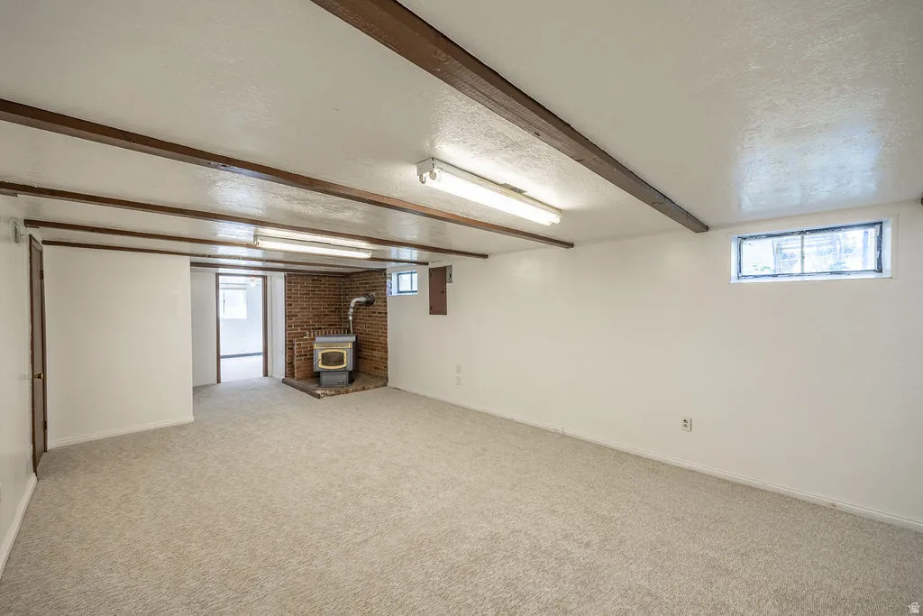 Spacious room with exposed wood ceiling beams, a brick fireplace surround, and a wood-burning stove