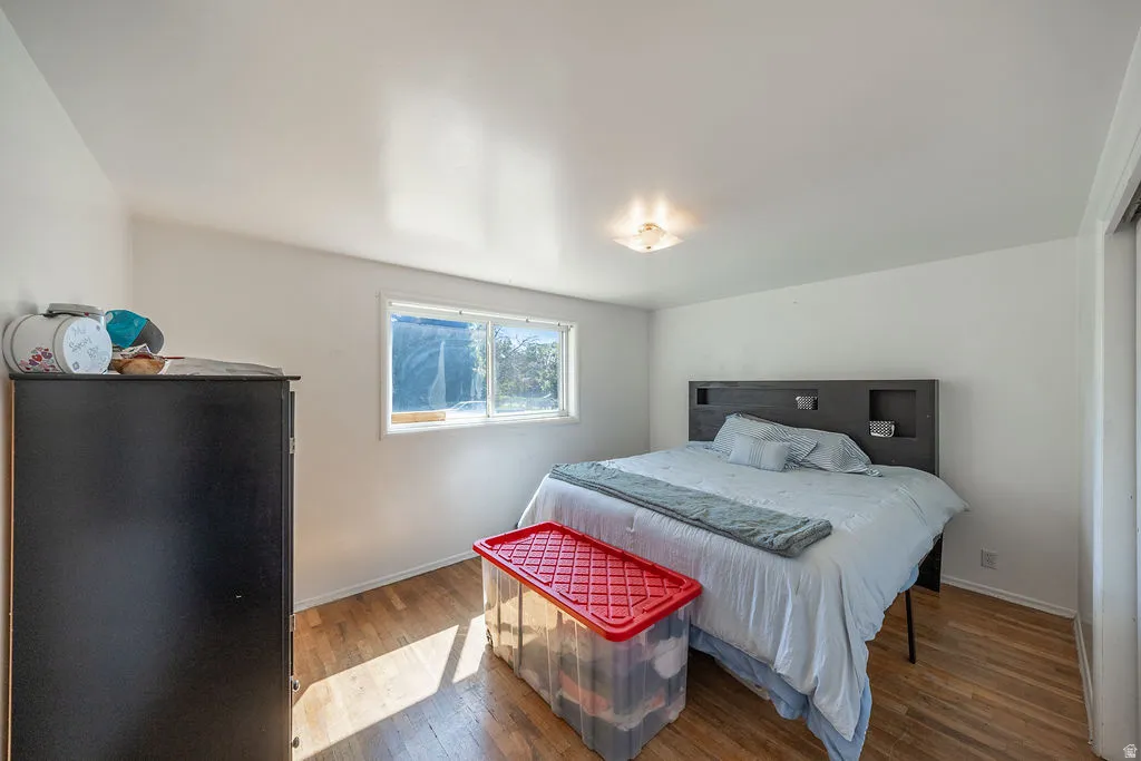 Hardwood flooring, white painted walls, window with natural light, flush mount ceiling light fixture, and a built-in closet with sliding doors