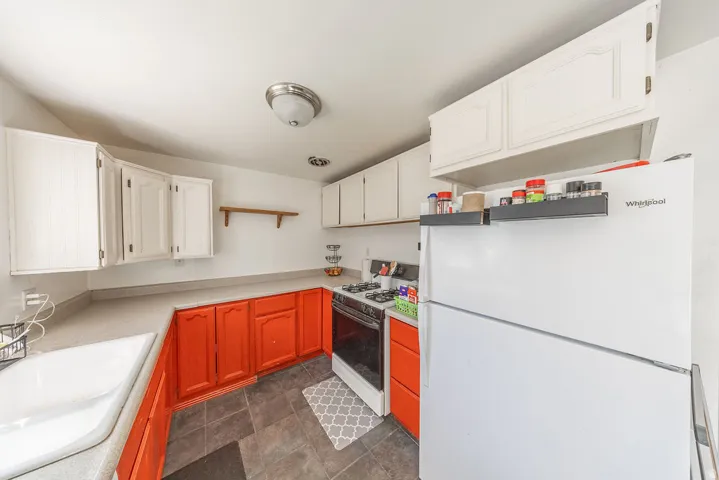 White upper cabinetry contrasting with orange lower cabinetry, light-toned countertops, and dark tile flooring