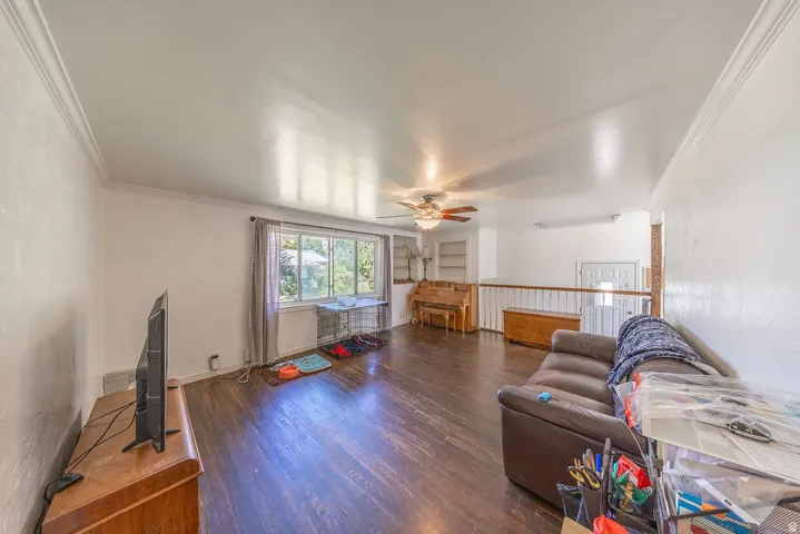 Hardwood-finish flooring, white painted walls, crown molding, ceiling fan, and large window