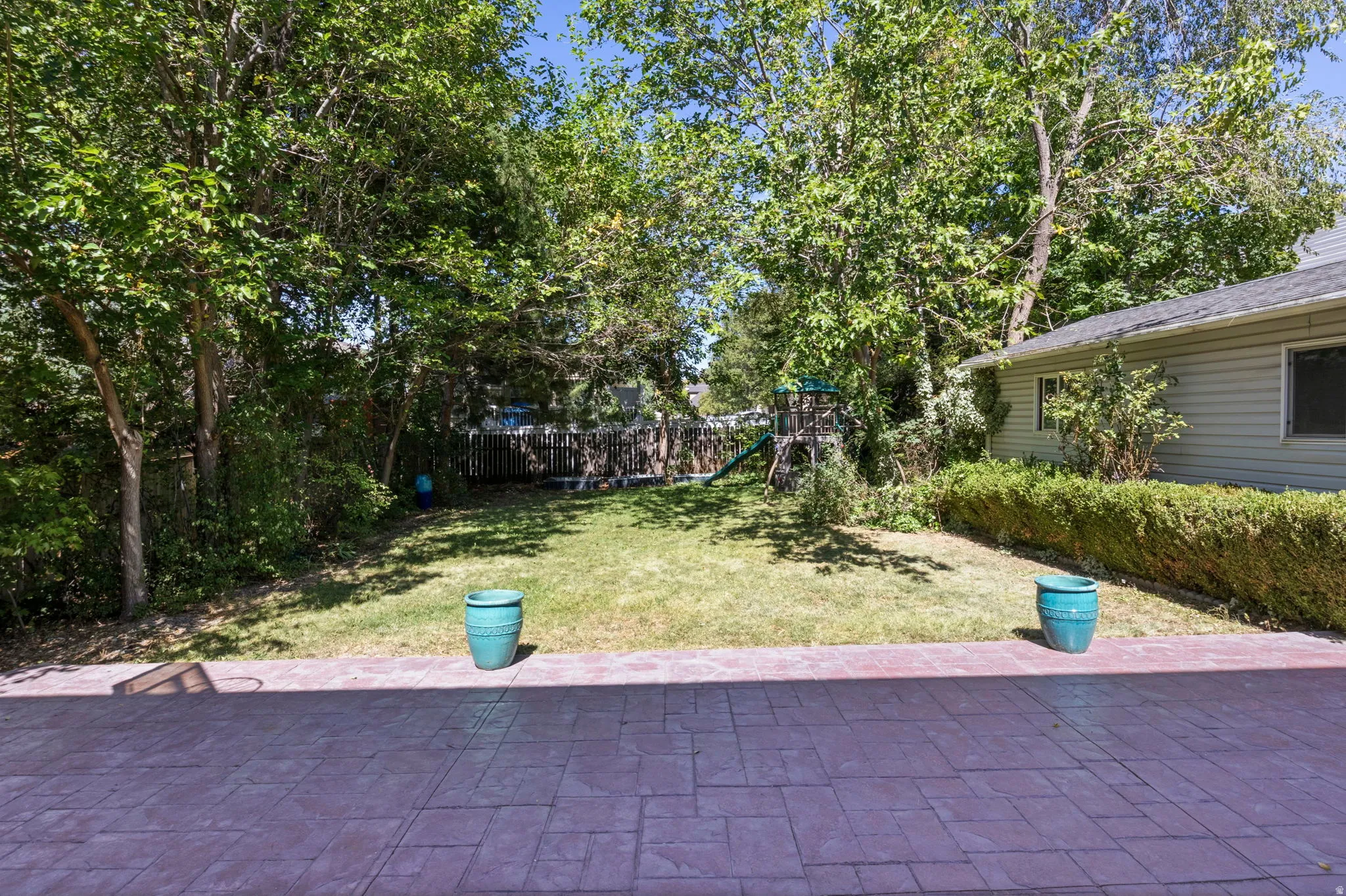Stamped concrete patio with a grassy yard, mature trees, and a low hedge border