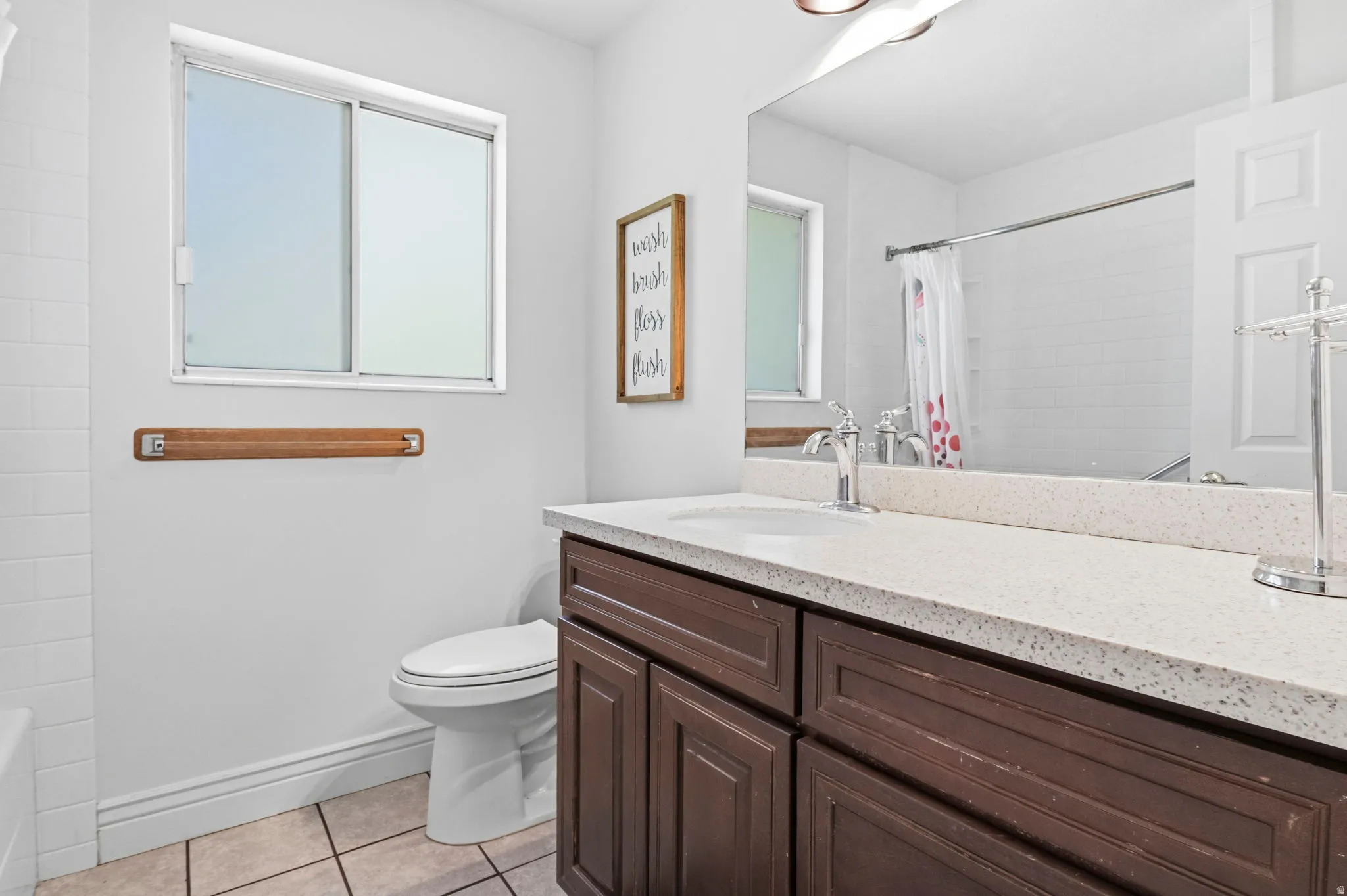 Bathroom vanity with a light-colored countertop and integrated sink, dark wood-finish cabinetry, and a framed mirror
