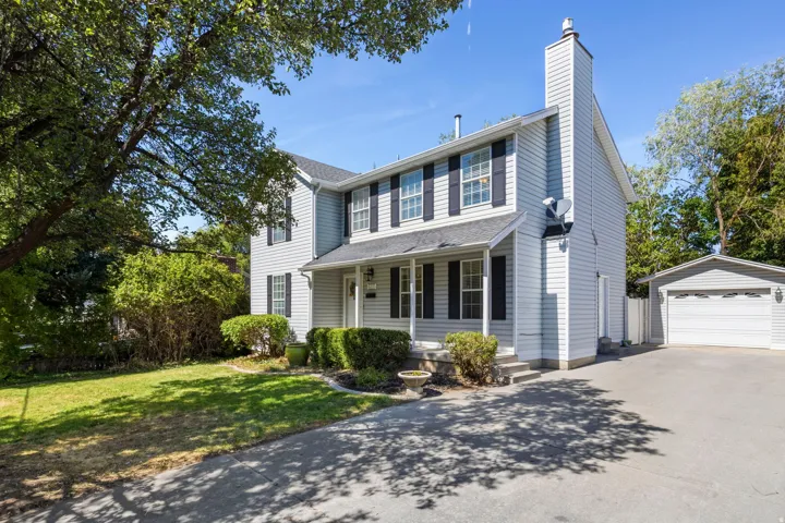 Two-story residence featuring light-colored siding, black window shutters, a prominent chimney, and a covered front porch