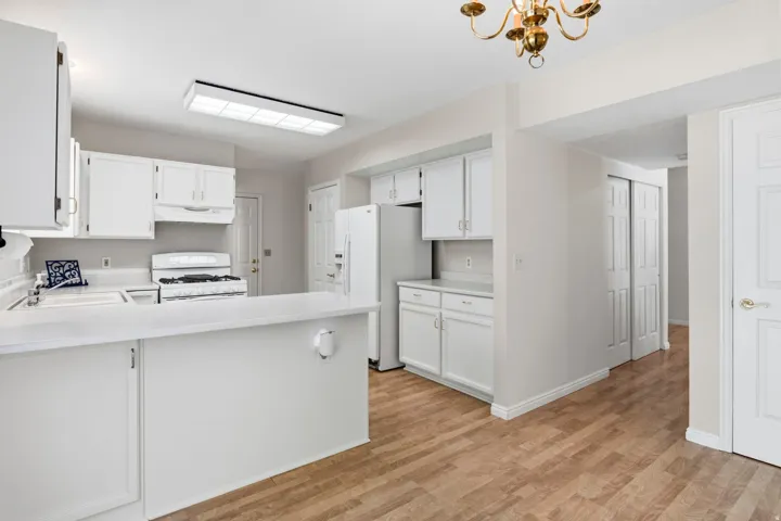 Kitchen featuring white cabinetry, white countertops, built-in appliances, wood-finish flooring, and a brass chandelier