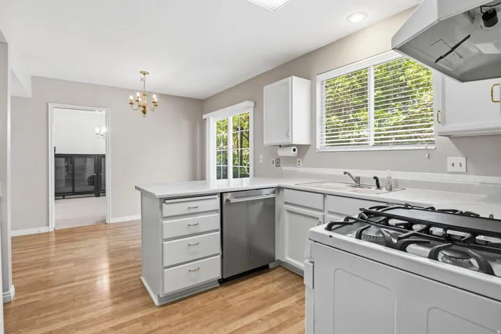 Kitchen featuring wood-finish flooring, white cabinetry, a stainless steel dishwasher, a gas range, and a breakfast bar