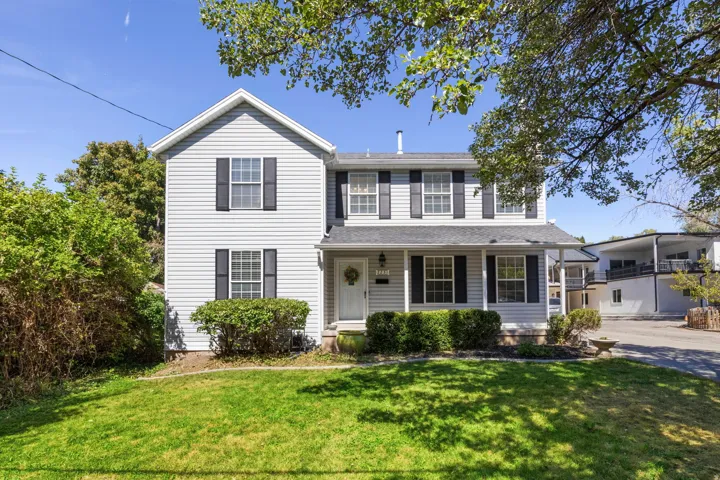 Two-story residence featuring light gray siding, a covered front porch, and black window shutters