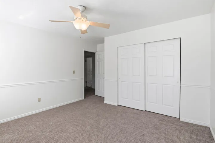 Neutral-toned carpet flooring, white walls with decorative chair rail molding, a ceiling fan with light fixture, and white sliding closet doors