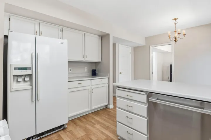 Kitchen featuring white cabinetry, light-toned countertops, wood-finish flooring, and a stainless steel dishwasher