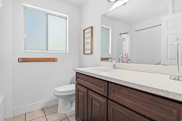 Bathroom vanity with a light-colored countertop and integrated sink, dark wood-finish cabinetry, and a framed mirror