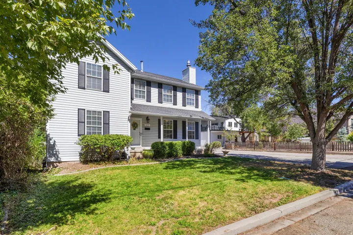 Two-story residence featuring white siding, dark shutters, a covered porch, a front lawn, and mature trees