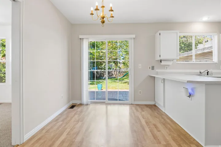 Wood-finish flooring with white baseboards, sliding glass patio door, and a traditional brass chandelier