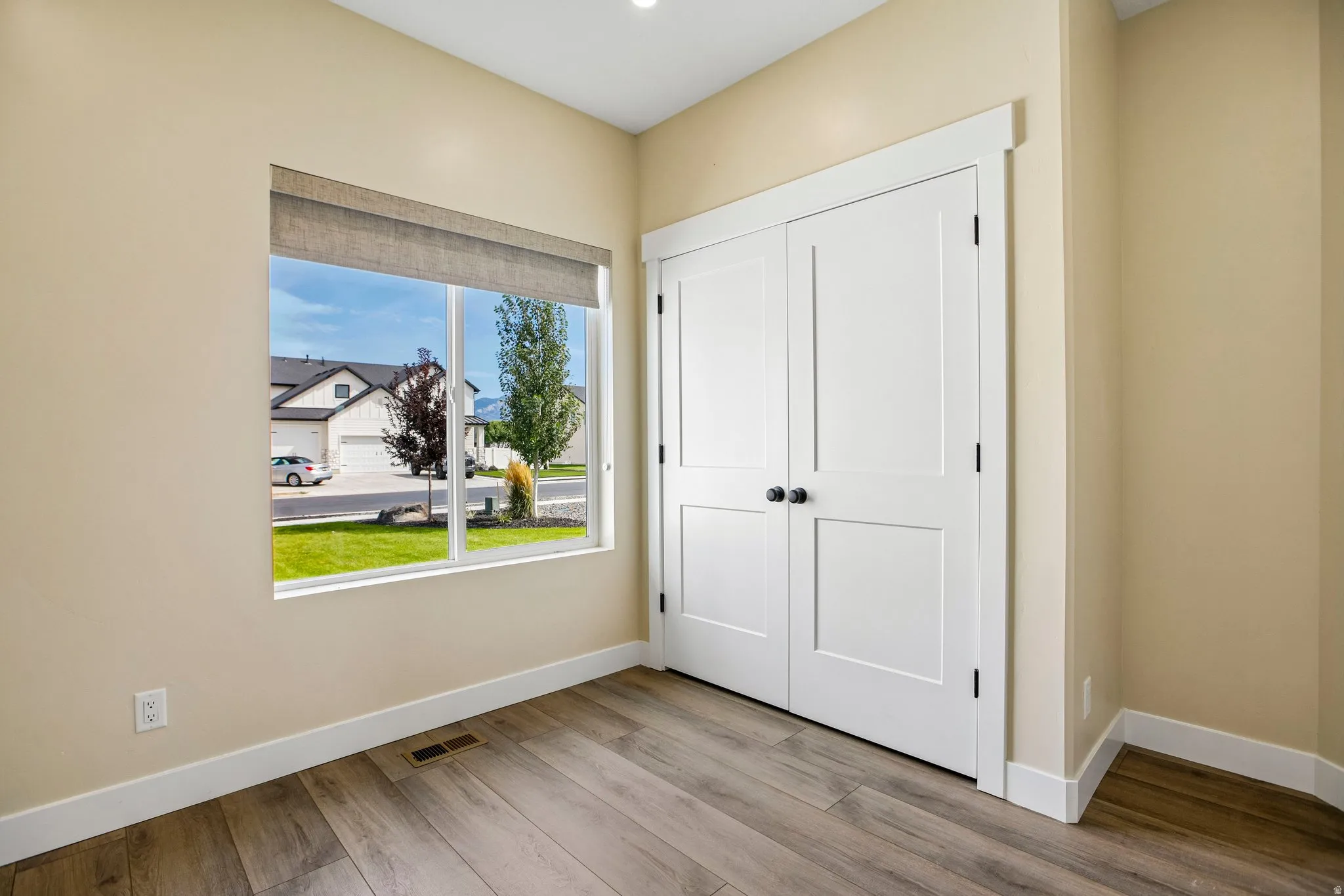 Wood-finish flooring throughout, white trim, and a window with a roller shade
