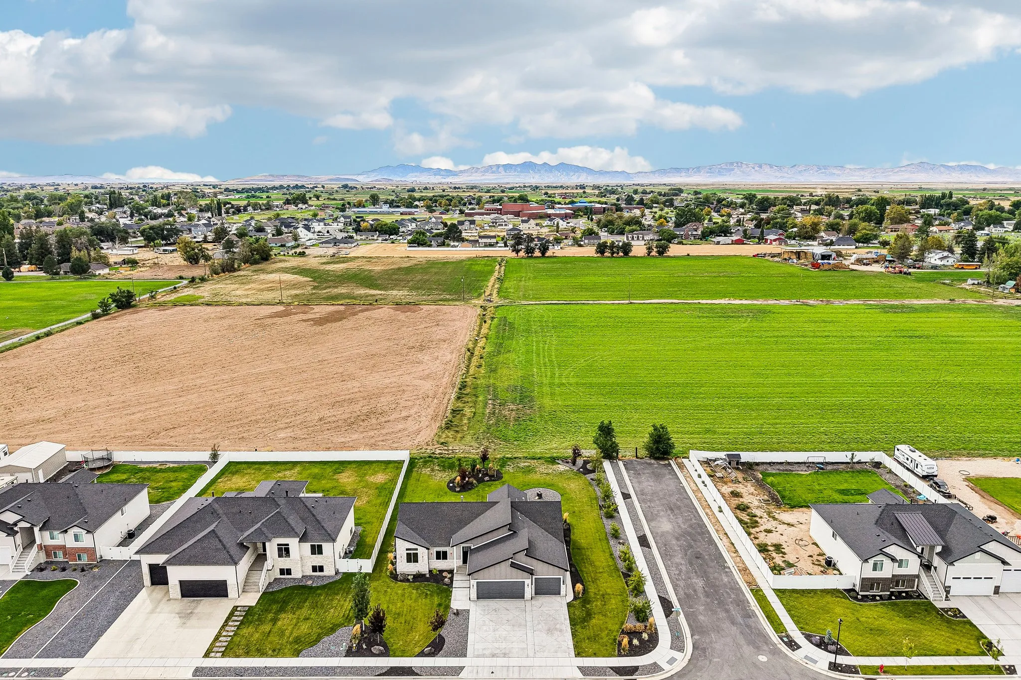 Modern residential development with a mountain backdrop, surrounded by expansive agricultural fields