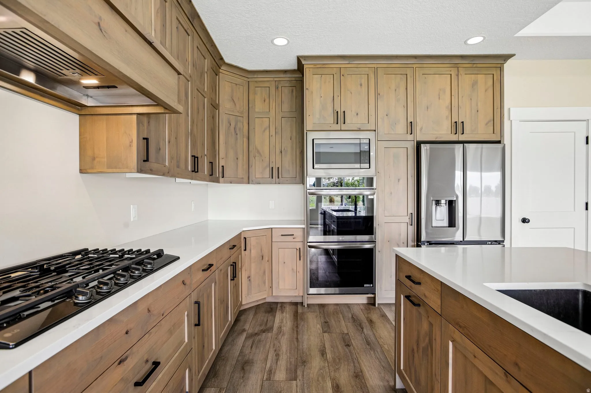 Light wood-finish cabinetry with black hardware, white countertops, built-in stainless steel appliances, and wood-finish flooring